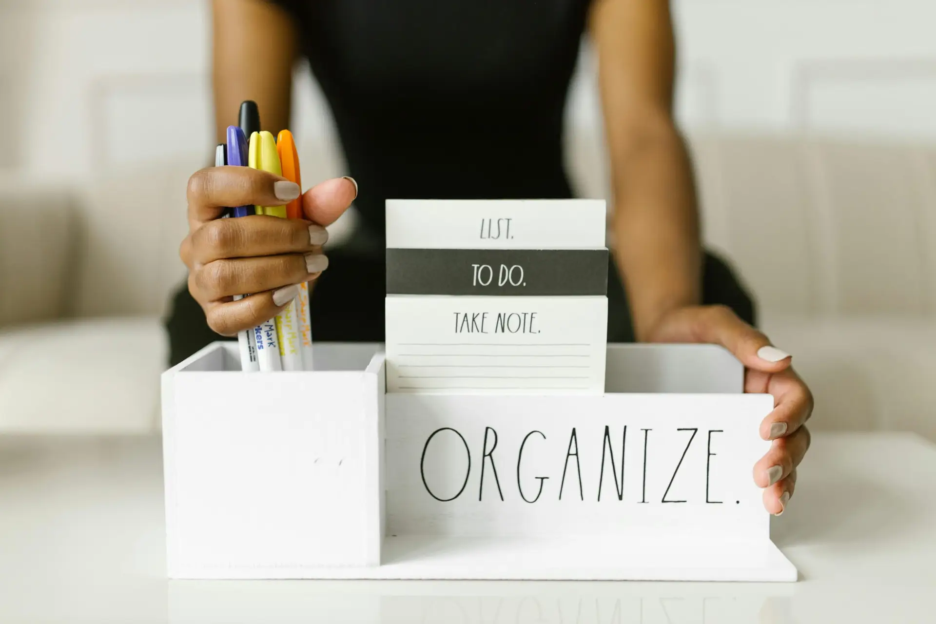 Close-up of hands organizing pens and notes in a white box labeled 'Organize.' Perfect for productivity inspiration.
